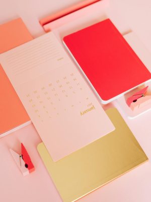 Layout of stylish notebooks with calendar paper and wooden clips on pink background